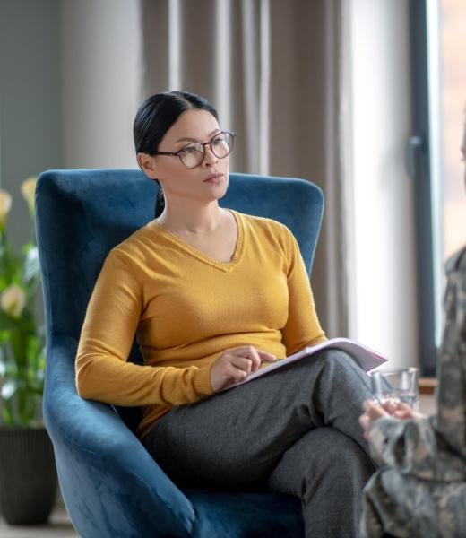 Psychoanalyst listening to woman wearing military uniform Asian psychoanalyst. Asian dark-haired psychoanalyst listening to woman wearing military uniform