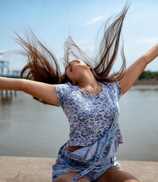 She Doesn’t Need Much To Have Fun A beautiful smiling young woman having fun with raised arms and enjoying on the city rivershore on a beautiful summer day.